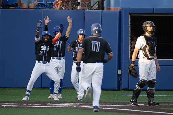 Baseball team members high five anther team member coming into home plate